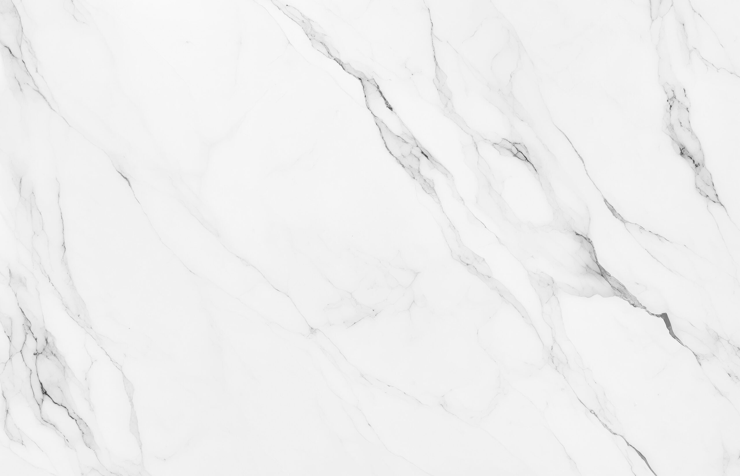 White marble surface with subtle gray veining running diagonally across. The smooth texture and organic pattern create an elegant, natural look. Light and shadow interplay enhances the depth of the veins, giving the marble a polished and refined appearance.